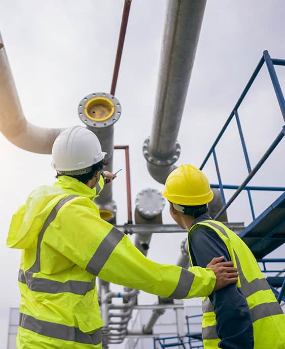 Two men in safety vests inspecting pipes at a construction site.